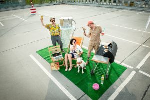 Das Ergebnis des Fotoshootings "Platz ist in der kleinesten Parzelle": Rollrasen in einer Parklücke, darauf feiern drei Menschen und ein Hund eine Grillparty.