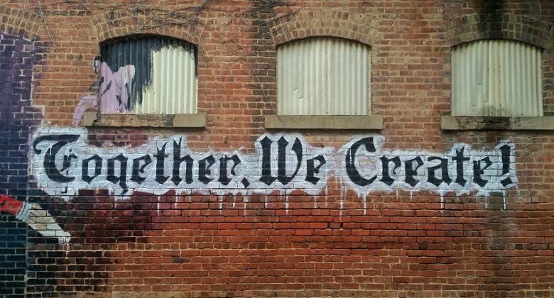 Backstein-Wand mit Graffiti "Together We Create!"
